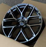 Glossy black Audi alloy wheel with silver accents, shown in a cardboard shipping box, front view