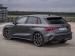 Rear three-quarter view of a gray Audi S3 sedan/wagon with large alloy wheels, parked on a rooftop parking lot under a cloudy sky.