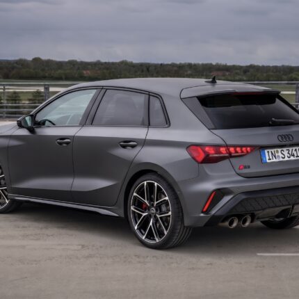 Rear three-quarter view of a gray Audi S3 sedan/wagon with large alloy wheels, parked on a rooftop parking lot under a cloudy sky.