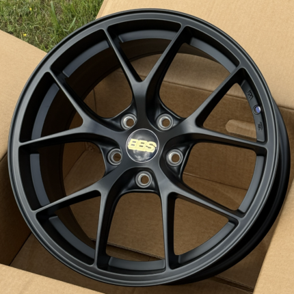 Black BBS alloy wheel with five split spokes resting on a cardboard box outdoors