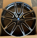 BMW M alloy wheel with a black-and-silver multi-spoke design and the BMW crest at the center, resting in a cardboard box.
