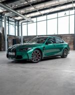 Emerald green BMW sedan parked in a warehouse-like space with large windows and metal ducts.