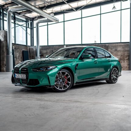 Emerald green BMW sedan parked in a warehouse-like space with large windows and metal ducts.
