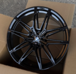 Glossy black BMW alloy wheel with a multi-spoke design resting in an open cardboard box, center cap shows BMW logo.