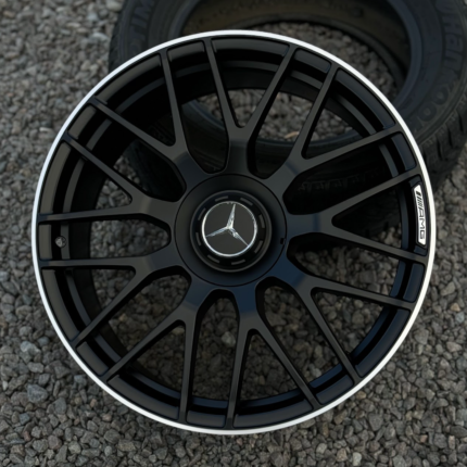 Close-up of a black multi-spoke Mercedes-AMG alloy wheel with a silver rim and central Mercedes emblem, resting on gravel.