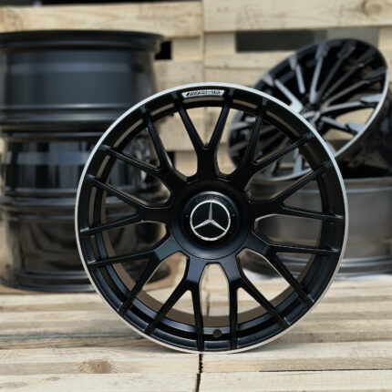 Close-up of a black Mercedes‑AMG alloy wheel with a silver lip, against a wooden pallet backdrop by stacked rims.