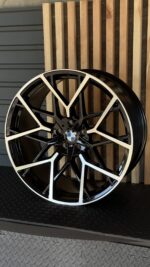 BMW alloy wheel with black spokes and white accents displayed against wooden slat backdrop