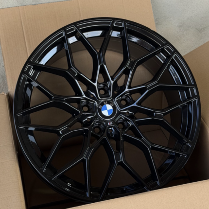 Black BMW alloy wheel with a blue-and-white center cap sitting in a cardboard box.