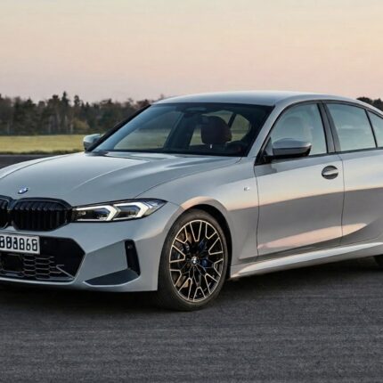 Front three-quarter view of a silver BMW sedan on an open road with a grassy field in the background, during sunset.