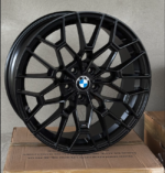 Black multi-spoke BMW alloy wheel with BMW roundel center, propped on a cardboard box.