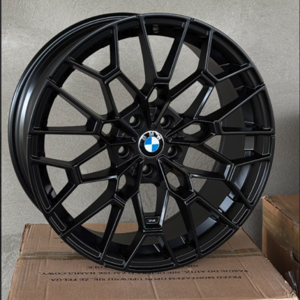 Black multi-spoke BMW alloy wheel with BMW roundel center, propped on a cardboard box.
