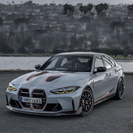 Silver BMW sports sedan with black and red racing stripes, parked on a paved road by a body of water.