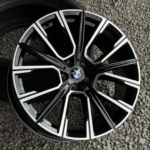 Close-up of a black and chrome BMW alloy wheel resting on gravel, with the BMW emblem at the center.