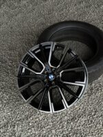 Close-up of a black and silver BMW alloy wheel with a mounted tire, resting on gray gravel.