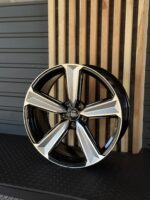 Close-up of an Audi alloy wheel with black and silver spokes, centered Audi emblem, in front of wooden slat panels.