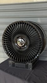 Close-up of a large black multi-spoke alloy wheel with a chrome center cap reading 'RANGE ROVER' on a dark stand.