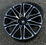 BMW alloy wheel with black and silver geometric spokes on a gravel surface, centered BMW logo.