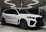 White BMW SUV parked in a garage with geometric, bright ceiling lights above it.