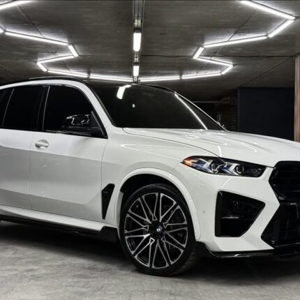 White BMW SUV parked in a garage with geometric, bright ceiling lights above it.