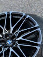 Close-up of a glossy black and silver BMW alloy wheel showing intricate spoke design and center BMW emblem on a car tire background, cropped edge view.