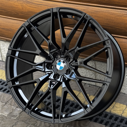 Black glossy BMW alloy wheel with a multi-spoke design and a blue-and-white BMW center badge, leaning against a wooden surface.