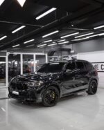 Black luxury SUV on a glossy showroom floor, front grille and yellow brake calipers visible.