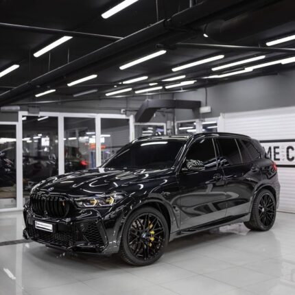 Black luxury SUV on a glossy showroom floor, front grille and yellow brake calipers visible.