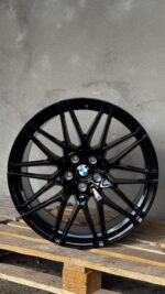 Black BMW alloy wheel with a multi-spoke design leaning on wooden pallets, logo at center