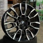 Black and silver BMW alloy wheel close-up, showing intricate spoke design and center badge on a tire in a showroom setting.] ,