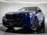 Blue BMW SUV (M badge) shown from a front three-quarter view with large kidney grille and sporty black wheels, on a showroom floor