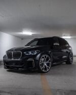 Front three-quarter view of a dark BMW SUV parked in an underground garage, showing large kidney grille and alloy wheels