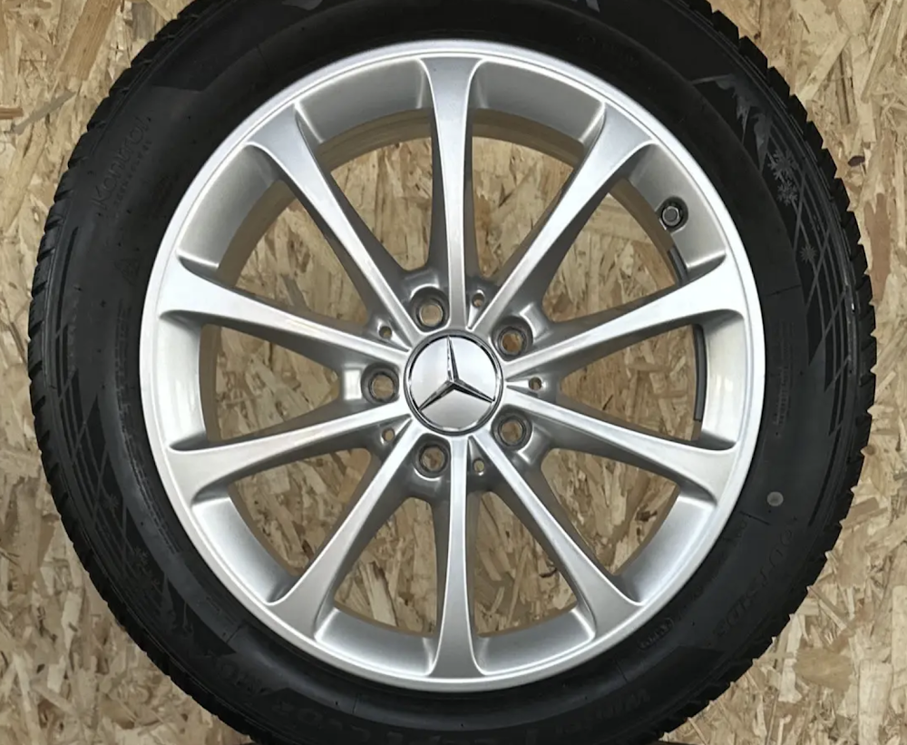 DSK-R17-5x112-f40fe9_0-1 Silver Mercedes alloy wheel with tire mounted, centered Mercedes emblem on a wooden background