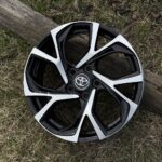 Toyota alloy wheel with black and silver spokes resting on grass beside a log.