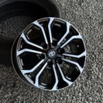 Close-up of a black and white multi-spoke alloy wheel with a Toyota center cap on a gravel surface