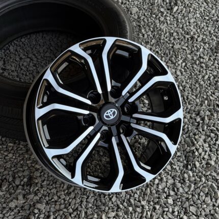 Close-up of a black and white multi-spoke alloy wheel with a Toyota center cap on a gravel surface