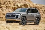 Silver Toyota SUV parked on sandy desert terrain with sandstone cliffs in the background