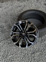 Black and silver alloy car wheel with Toyota emblem resting on a tire on a gravel surface