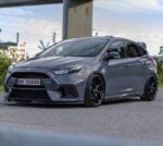 Gray Ford Focus RS hatchback in a front three-quarter view, parked on a paved surface with black alloy wheels and blue brake calipers (license plate NF 90000).