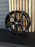 Glossy black alloy wheel with a multi-spoke design and a Ford center cap, resting against wooden slats.