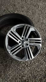 Close-up of a silver multi-spoke alloy wheel with a black tire, resting on gravel; VW logo at center.
