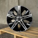 Mercedes-Benz alloy wheel with a black and silver split-spoke design resting on a wooden pallet outdoors.