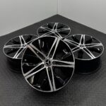 Four Mercedes-Benz alloy wheels with a black and silver five-spoke design, arranged on a dark textured floor.