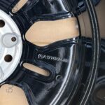 Close-up of a glossy black car wheel rim with stamped numbers and cutouts, showing a brown inner surface.
