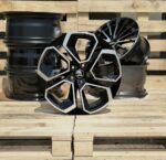 Black and silver alloy car wheel resting on a wooden pallet with other rims in the background