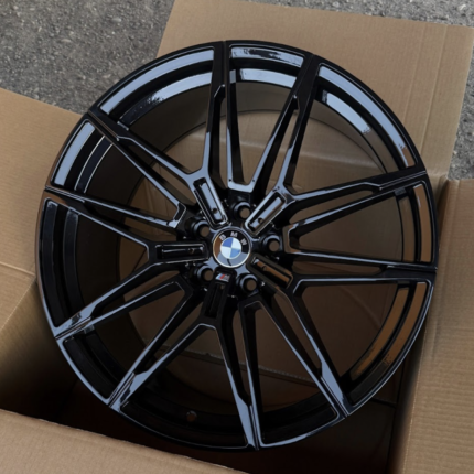 Glossy black BMW alloy wheel with a multi-spoke design, placed inside an open cardboard box with the BMW center cap visible