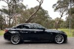 Black luxury sedan parked on a quiet road with trees in the background.