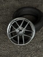 Chrome multi-spoke alloy wheel resting on gravel with a tire in the background.