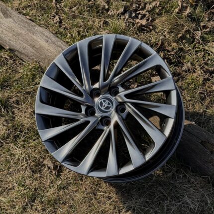 Silver Toyota alloy wheel resting on grass, with multiple spokes and a central Toyota emblem visible.