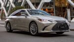 Silver Lexus ES300h sedan parked on a city street with a modern glass building in the background, daytime.