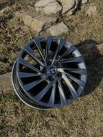 Metallic grey Toyota alloy wheel lying on dry grass and rocks, detached from a vehicle, vented spokes visible.